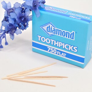 May include: A blue box of Diamond toothpicks with 750 flat toothpicks. The box is on a white surface with a blue flower.