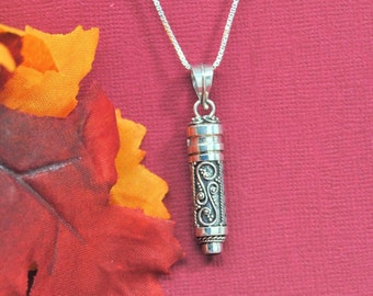May include: A silver pendant necklace with a detailed, ornate, cylindrical charm. The charm has a filigree design and appears to be a small container.