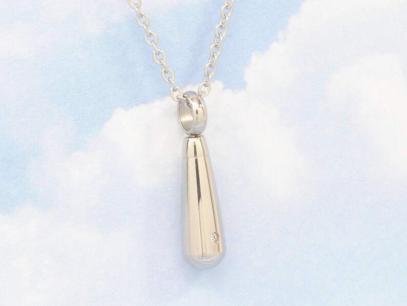 May include: A silver teardrop-shaped pendant necklace with a small diamond accent. The necklace is on a silver chain.