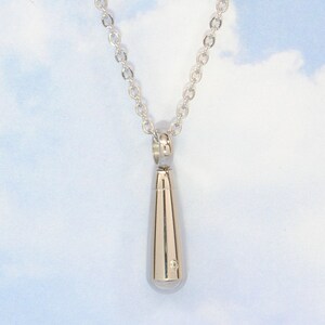 May include: A silver teardrop-shaped pendant necklace with a small diamond accent. The necklace is on a silver chain.