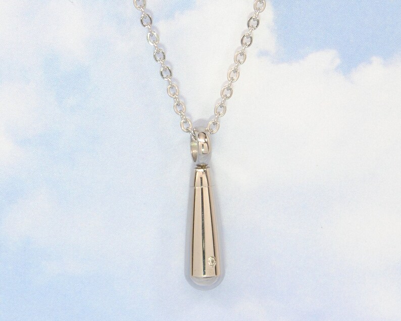 May include: A silver teardrop-shaped pendant necklace with a small diamond accent. The necklace is on a silver chain.