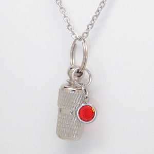 May include: A silver chain necklace with a small silver cylinder pendant and a red crystal charm. The cylinder pendant has a threaded design.