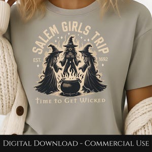 May include: A light gray t-shirt featuring a graphic of three witches around a cauldron with flames. The text reads "SALEM GIRLS TRIP" and "TIME TO GET WICKED". The design includes the year "1692" and the text "EST."