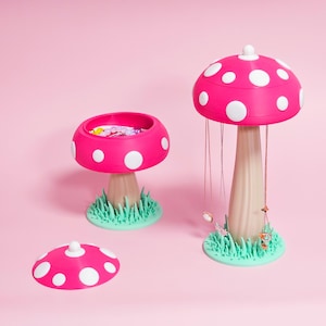 May include: A whimsical jewelry organizer set featuring three mushroom-shaped pieces. The set includes a large mushroom with hanging necklaces, a smaller mushroom with a storage bowl, and a mushroom lid. The mushrooms are bright pink with white polka dots, beige stems, and green grass bases.