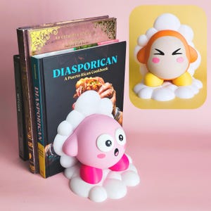 May include: A pink and white cartoon character bookend with a surprised expression, holding up a stack of books. The books include "DIASPORICAN A Puerto Rican Cookbook". A second character is on a yellow background.