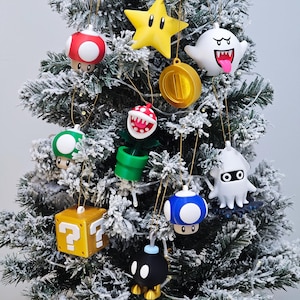 May include: A collection of hanging ornaments featuring various video game characters and items, including a yellow star, a white ghost, a red mushroom, a green mushroom, a blue mushroom, a piranha plant, a gold question block, a gold coin, a squid, and a black bomb.