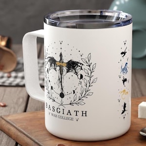 May include: White travel mug with a black and white illustration of a dragon with stars and moons. The text "Basgiath War College" is printed below the dragon.