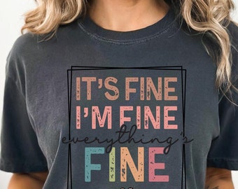 May include: A dark gray t-shirt with a colorful graphic that says "It's Fine I'm Fine Everything's Fine".