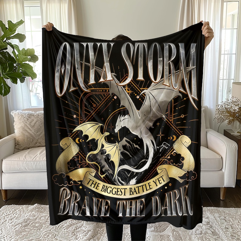 May include: Black throw blanket featuring a white dragon and gold accents. The text "Onyx Storm" and "Brave the Dark" is printed on the blanket.