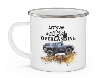 May include: White enamel camping mug with a silver rim. The mug features a black and white illustration of a 4x4 vehicle driving through a mountainous landscape. The text "Let's Go Overlanding" is printed in black on the mug.