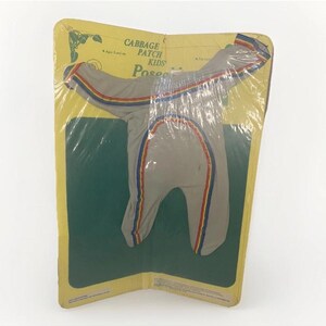 May include: Vintage Cabbage Patch Kids Poseable doll clothing set, still in its original packaging. The outfit is gray with red, yellow, and blue stripes. The packaging is yellow and green.