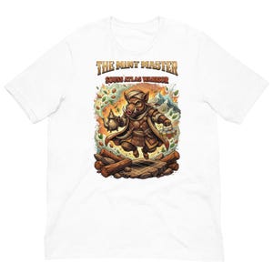 May include: White t-shirt featuring a cartoon illustration of a boar warrior holding a teapot and bottles. The text "THE MINT MASTER SOUSS ATLAS WARRIOR" is printed above the illustration in a gold color. The boar is wearing a brown robe and turban.