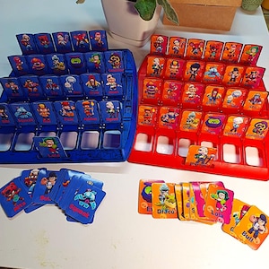 May include: Two board game sets, one blue and one red, with character cards. The blue set has blue cards with character illustrations. The red set has orange cards with character illustrations. Several character cards are also visible.