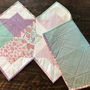 K&ouml;nnte beinhalten: Zwei gesteppte Babydecken, eine mit einem gr&uuml;n-wei&szlig;en Tupfenmuster und die andere mit einem Patchwork-Design mit rosa, lila und gr&uuml;nen Blumenmustern.