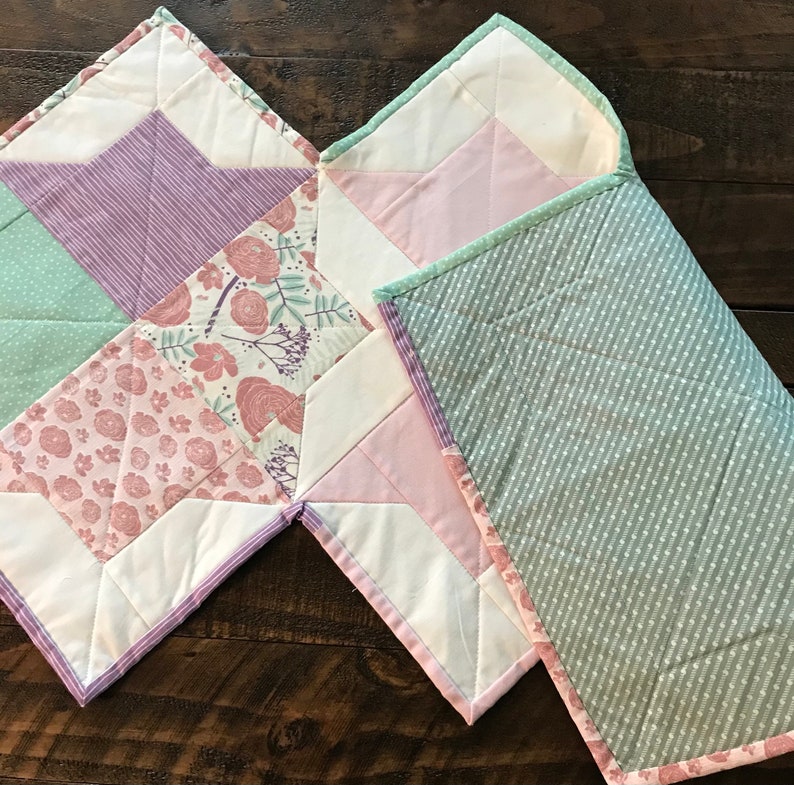 K&ouml;nnte beinhalten: Zwei gesteppte Babydecken, eine mit einem gr&uuml;n-wei&szlig;en Tupfenmuster und die andere mit einem Patchwork-Design mit rosa, lila und gr&uuml;nen Blumenmustern.