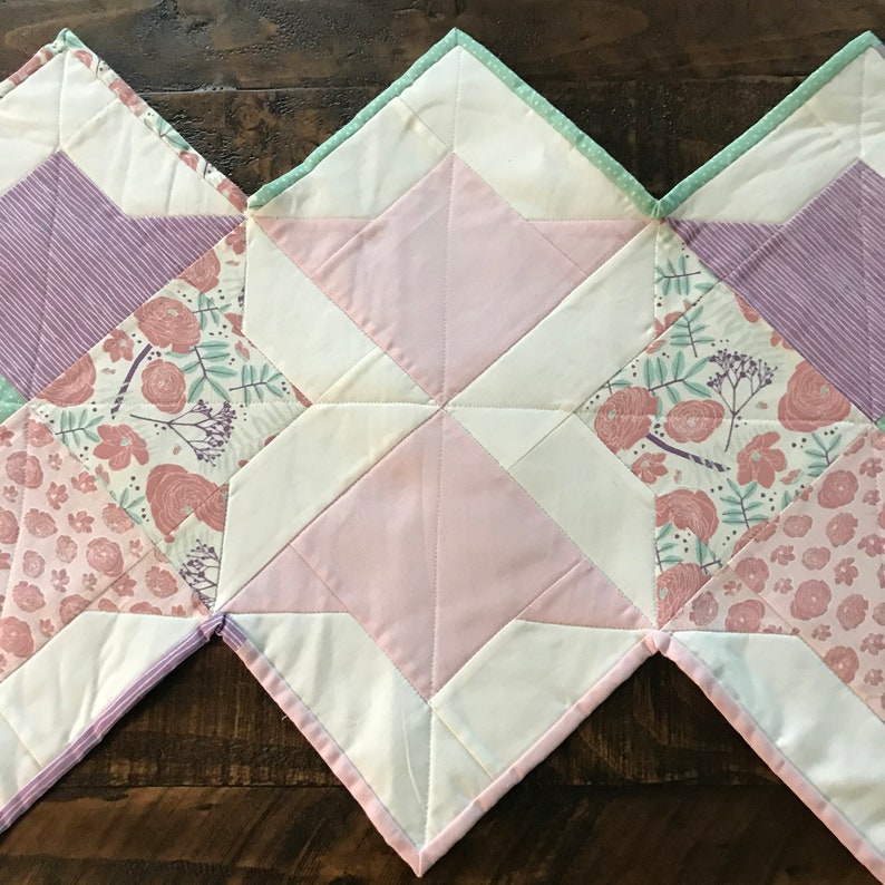 K&ouml;nnte beinhalten: Ein rosafarbener, wei&szlig;er und gr&uuml;ner Patchwork-Quilt-L&auml;ufer mit geometrischem Muster. Der L&auml;ufer besteht aus verschiedenen Stoffen mit Blumen- und Streifenmustern.