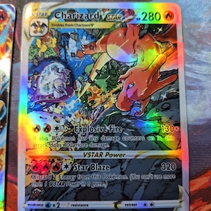 May include: A holographic Charizard VSTAR Pokémon card. The card features a vibrant illustration of Charizard in a dynamic pose, with the text "Charizard VSTAR" and attack details. The card has a HP of 280 and a Star Blaze attack of 320.