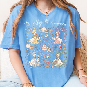 May include: Light blue t-shirt with the text "to silly to measure." The shirt features a whimsical design of cartoon geese in chef hats and aprons, surrounded by baking-related illustrations like teapots, scales, and rolling pins.