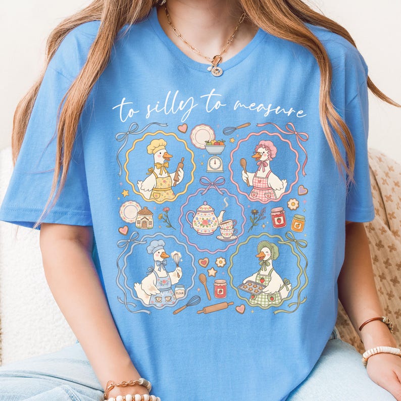 May include: Light blue t-shirt with the text "to silly to measure." The shirt features a whimsical design of cartoon geese in chef hats and aprons, surrounded by baking-related illustrations like teapots, scales, and rolling pins.