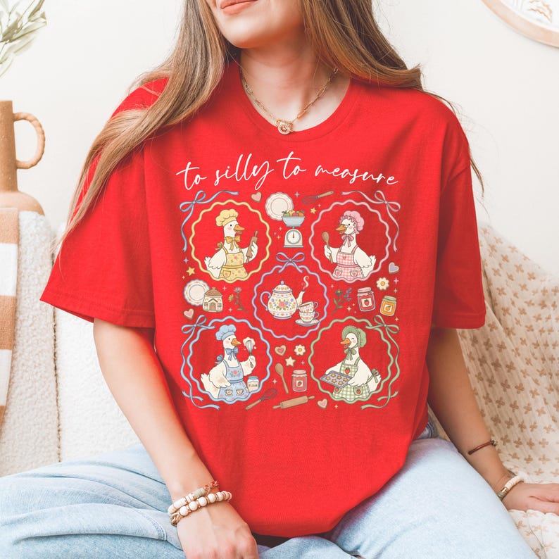 May include: Red t-shirt with the phrase "to silly to measure" in cursive. The shirt features a whimsical design of cartoon geese in chef hats and aprons, surrounded by kitchen-themed illustrations.