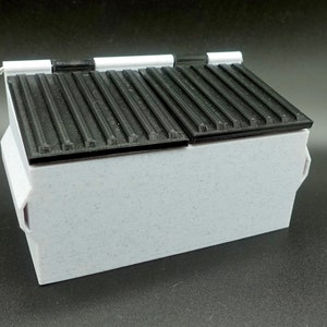 Könnte beinhalten: Ein weißer Plastik-Abfalleimer mit zwei schwarzen Deckeln. Die Deckel haben eine gerippte Textur und sind mit Scharnieren versehen.