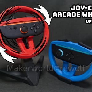 Puede incluir: Volantes arcade Joy-Con2 rojos y azules para una consola de juegos. El volante rojo se muestra con un gráfico de movimiento. El texto "JOY-CON2 ARCADE WHEEL UPDATED" se muestra encima de los volantes. Los volantes están sobre un soporte negro.