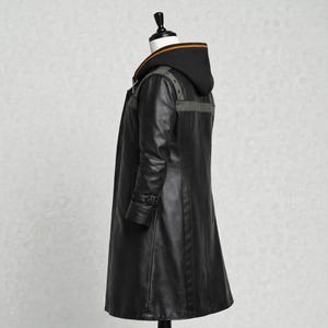 May include: A long black leather coat with a hood. The coat has a button closure, a belt detail on the sleeves, and grey accents on the shoulders and back. The hood has an orange stripe along the top edge.