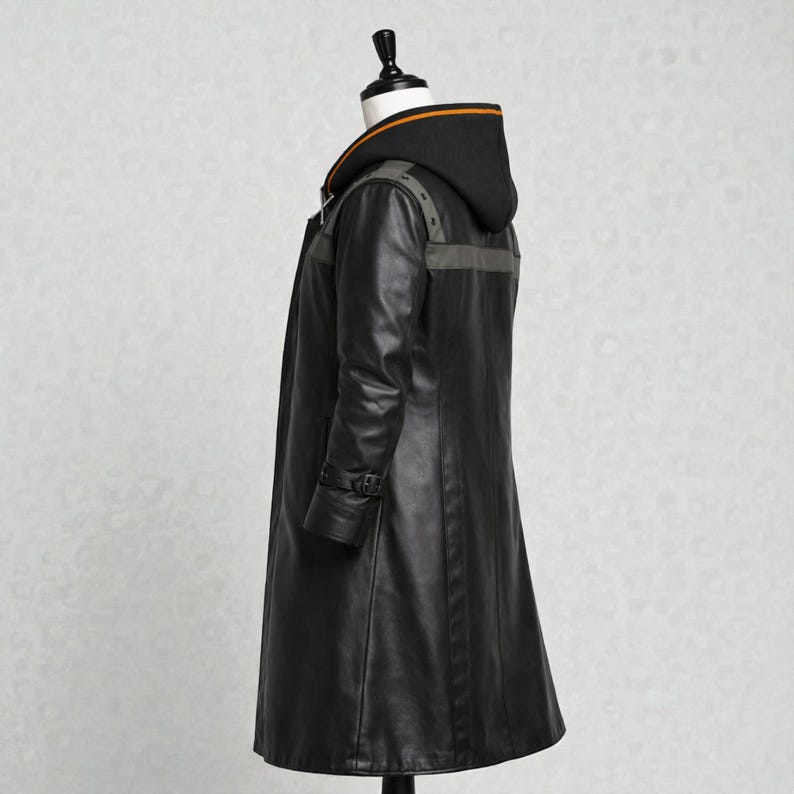 May include: A long black leather coat with a hood. The coat has a button closure, a belt detail on the sleeves, and grey accents on the shoulders and back. The hood has an orange stripe along the top edge.