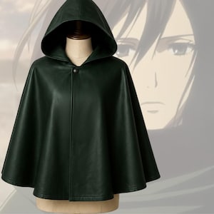 May include: A dark green hooded cloak with a single button closure. The cloak is displayed on a mannequin and has a smooth, leather-like texture. The background features a faded anime-style illustration.