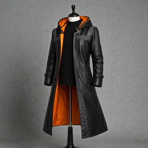 May include: A long black leather coat with an orange lining and hood. The coat has a high collar, a cross-shaped clasp, and grey shoulder accents. The coat is displayed on a mannequin.