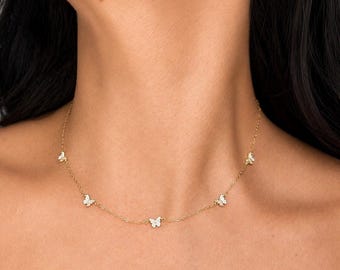 May include: A gold chain necklace featuring five evenly spaced butterfly charms. Each butterfly charm is embellished with small, clear, sparkling stones. The necklace rests around the neck, showcasing a delicate link chain design in a bright gold tone.