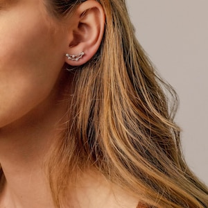 May include: A pair of silver earrings with a delicate chain design. The earrings are shaped like a crescent moon and feature small, sparkling stones.