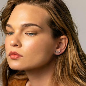 May include: A woman with long brown hair wearing a brown shirt and a small silver earring with a curved design.