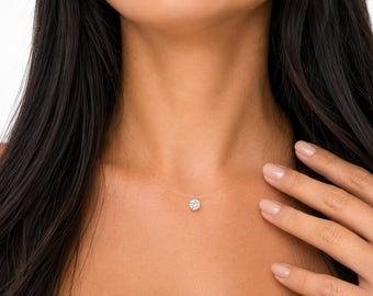 May include: A clear, thin nylon cord necklace featuring a single, round, brilliant-cut white gemstone pendant centered at the base of the neck. The transparent cord creates a floating effect for the sparkling, faceted stone setting.