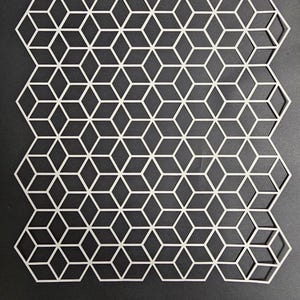 May include: A white geometric pattern cut from a single sheet. The design features a repeating pattern of interconnected three-dimensional cubes. The object is set against a dark background, highlighting the intricate design.
