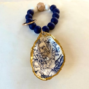 May include: A blue and white beaded keyring with a gold-rimmed oyster shell charm featuring a blue and white floral design.