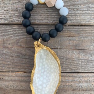 May include: A black and white beaded keyring with a gold-rimmed oyster shell charm. The keyring features a wooden bead and a gold key ring.