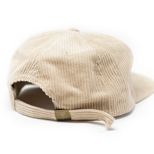 May include: A beige corduroy baseball cap with a curved brim. The cap has a brown adjustable strap in the back.