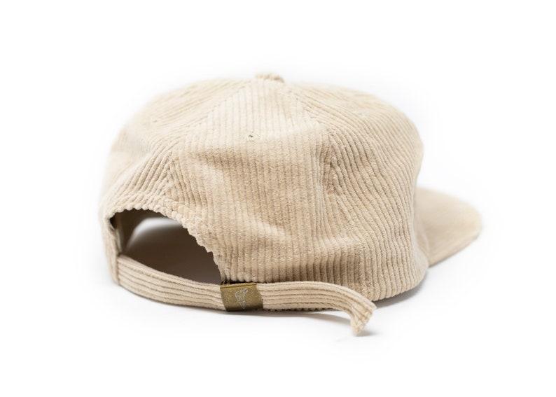 May include: A beige corduroy baseball cap with a curved brim. The cap has a brown adjustable strap in the back.