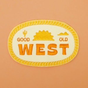 Könnte beinhalten: Ein gestickter Aufnäher in Gelb und Orange mit den Worten "Good Old West" in einem weißen Oval mit einem Seilrand. Der Aufnäher zeigt einen Kaktus, eine Sonne und einen Berg.