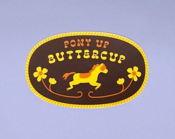 May include: A brown oval sticker with a yellow rope border. The sticker has a yellow horse with an orange mane and tail, and the text "Pony Up Buttercup" in orange and yellow letters.