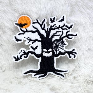 Op de afbeelding: Een zwart-wit Halloween-patch met een spookachtige boom met een gesneden gezicht, vleermuizen en een spinnenweb. Een oranje maan met een vleermuissilhouet staat linksboven. De patch heeft een witte geborduurde rand.