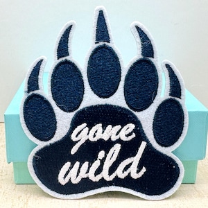May include: Embroidered patch in the shape of a bear paw with the words "gone wild" in white script. The paw print is navy blue with a white border. The patch is on a light blue box.
