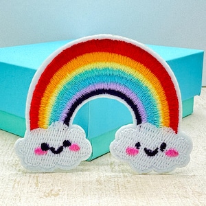 May include: An embroidered patch in the shape of a rainbow arching over two white clouds. The rainbow features bands of red, orange, yellow, green, blue, and purple thread. Each cloud has a stitched black smiling face and pink circular cheeks.