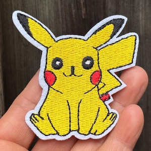 Könnte beinhalten: Gestickter gelber Pikachu-Aufnäher mit schwarzen Akzenten auf Ohren, Augen und Umriss. Der Aufnäher hat rote Wangenkreise und einen weißen Rand. Das Design ist eine Zeichentrickfigur aus dem beliebten Pokémon-Franchise.
