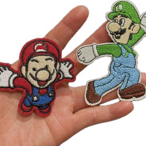 May include: Two embroidered fabric patches featuring iconic video game characters. One patch depicts a character in a red cap and blue overalls with arms outstretched. The second patch shows a character in a green cap and blue overalls running.