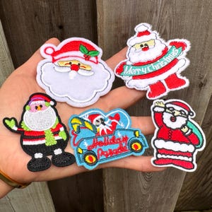 Puede incluir: Un conjunto de parches bordados con temática navideña que representan a Papá Noel en varias poses. Los parches son principalmente rojos, blancos y negros, con acentos verdes y amarillos. Un parche tiene el texto "Merry Christmas" en una pancarta.