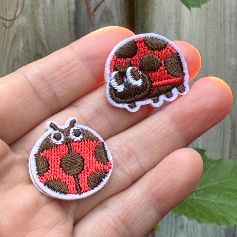 May include: Two embroidered ladybug patches. Each patch features a red body with brown spots and a white border. One ladybug has a smiling face. These patches are ideal for decorating clothing or accessories.