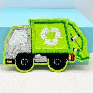 May include: Green and grey embroidered patch of a recycling truck with a white recycling symbol on the side.