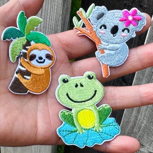May include: Three embroidered patches: a sloth hanging from a palm tree, a koala with a pink flower, and a green frog on a blue lily pad. The patches are colorful and feature detailed stitching, perfect for adding to clothing or accessories.